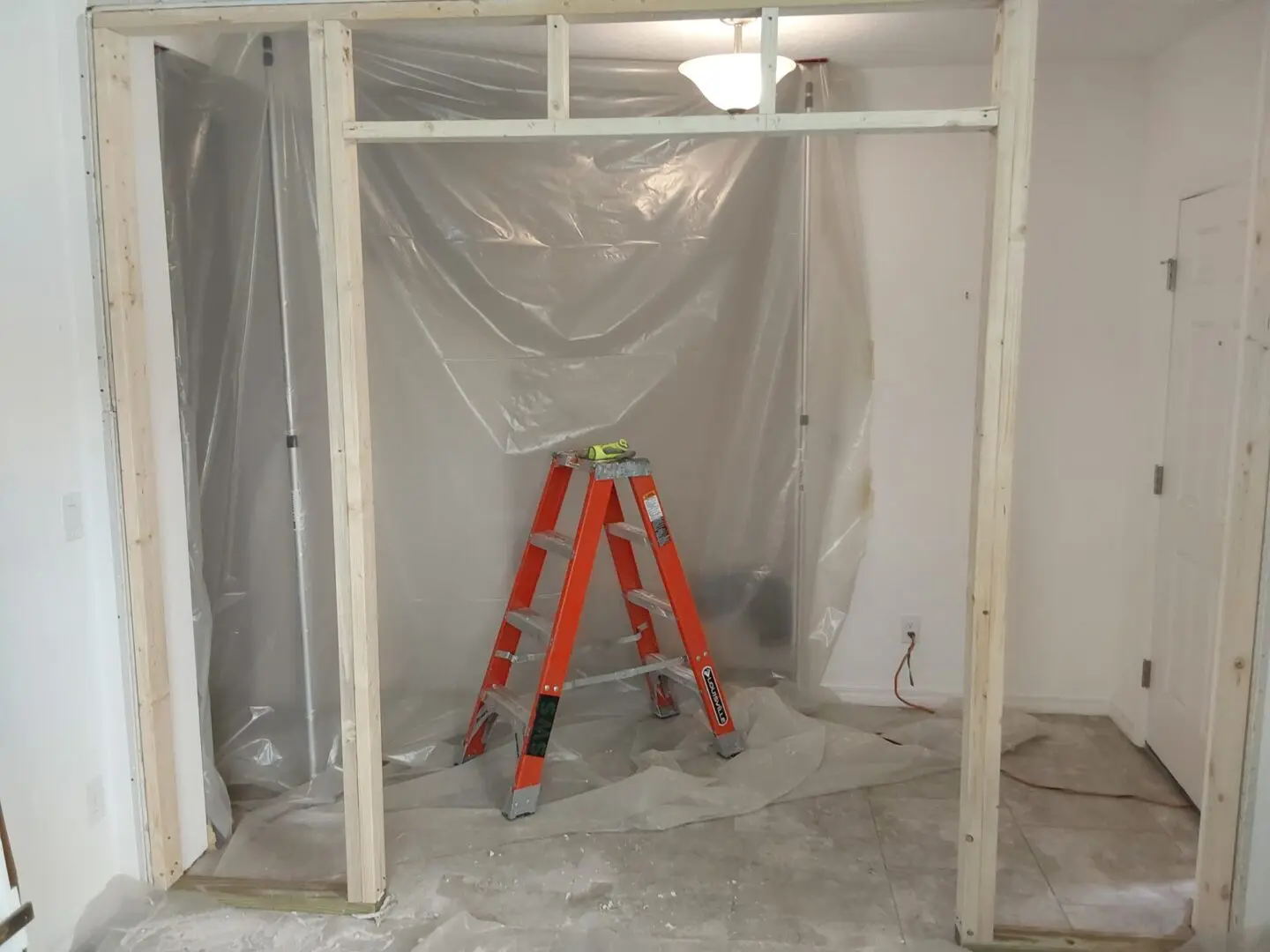 A ladder in the middle of a room with some plastic sheeting on it.