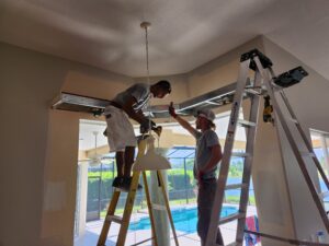 Two men working on a ceiling in a room.